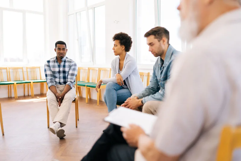 Two men and a woman in a group therapy session with addiction counselor