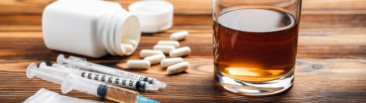 A glass of alcohol with pills and a syringe next to it.