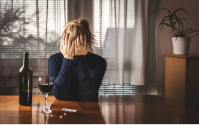 Distressed woman holds head in hands with a bottle of wine and pills in front of her