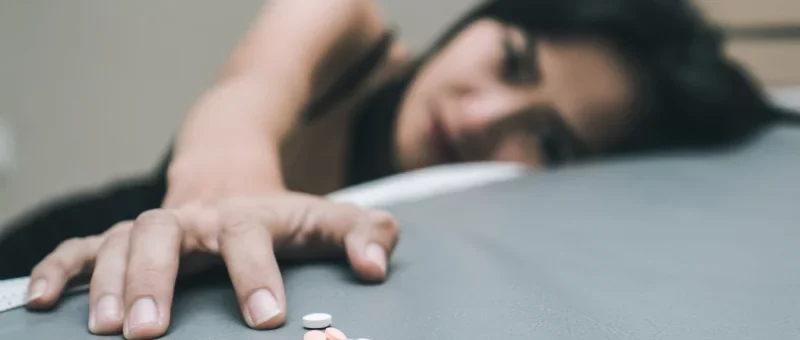 Young sad looking woman reaches for a pile of pills