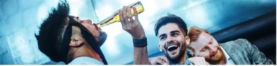 Young, drunk man with tie tied around his head chugs a beer with two friends