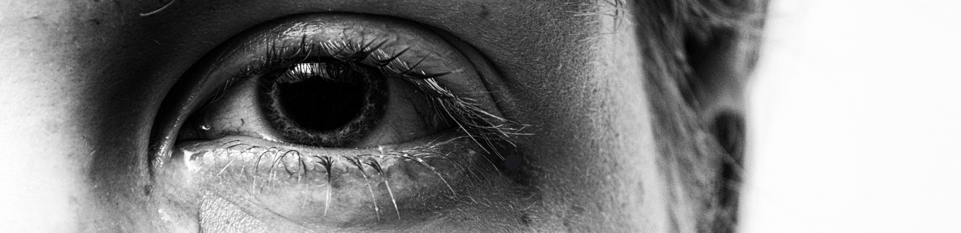 Blac and white closeup of an eye with a tear falling.