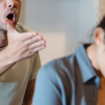 A man who has recently had alcohol appears to be angrily shouting and gesturing towards a woman, who looks distressed and is turning away with her head down.