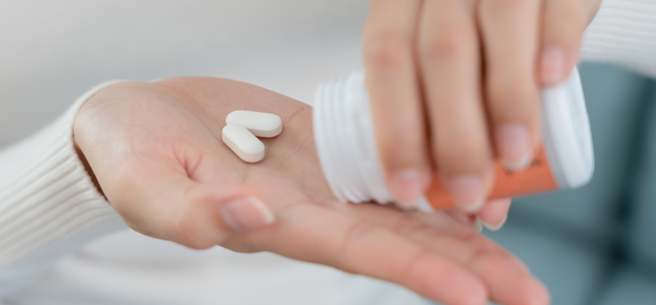 Close-up of a person's hand holding two benzos, poured from an orange prescription bottle. The person is wearing a white sweater, and the background is blurred