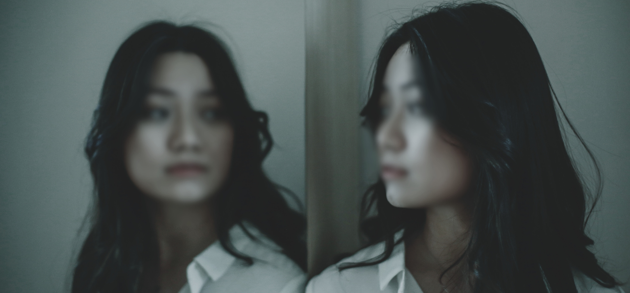 Woman looking at a blurred reflection of herself as she bears the emotional weight of the past and wonders how to forgive yourself